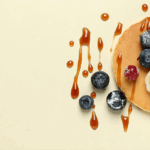 Banaan-ei pannenkoek met blauwe bessen, banaan en siroop op beige achtergrond.